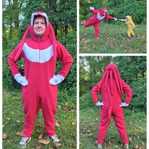 May include: Three people wearing red and yellow costumes with long tails. The costumes are inspired by the video game character Knuckles the Echidna. The people are standing in a grassy area with trees in the background.