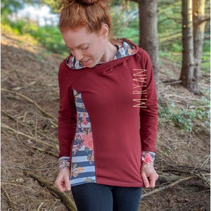 May include: A maroon long-sleeved hooded sweatshirt with a floral and striped pattern on the side panel. The sweatshirt has a  "M.RYAN" logo on the right sleeve.