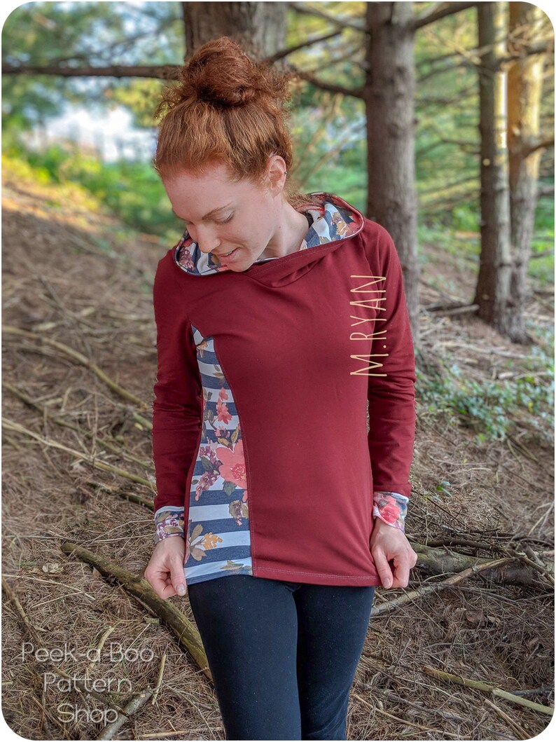May include: A maroon long-sleeved hooded sweatshirt with a floral and striped pattern on the side panel. The sweatshirt has a  "M.RYAN" logo on the right sleeve.
