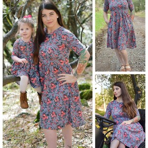 Pode incluir: Duas pessoas vestindo vestidos combinando com estampa floral. O vestido &eacute; cinza com flores rosa e vermelhas. O vestido tem mangas curtas e um decote redondo. O vestido &eacute; at&eacute; o joelho. As pessoas est&atilde;o em p&eacute; em uma &aacute;rea arborizada.