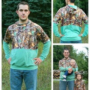 May include: A long-sleeved hooded sweatshirt with a camouflage print on the top half and a solid teal colour on the bottom half. The sweatshirt is shown being worn by three people, including a child.