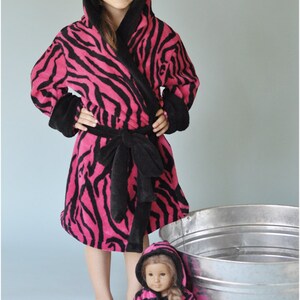 May include: A pink and black zebra print robe with a hood and a matching belt. A smaller doll is wearing a similar robe. The text "Peek-a-Boo Pattern Shop" is visible at the bottom of the image.