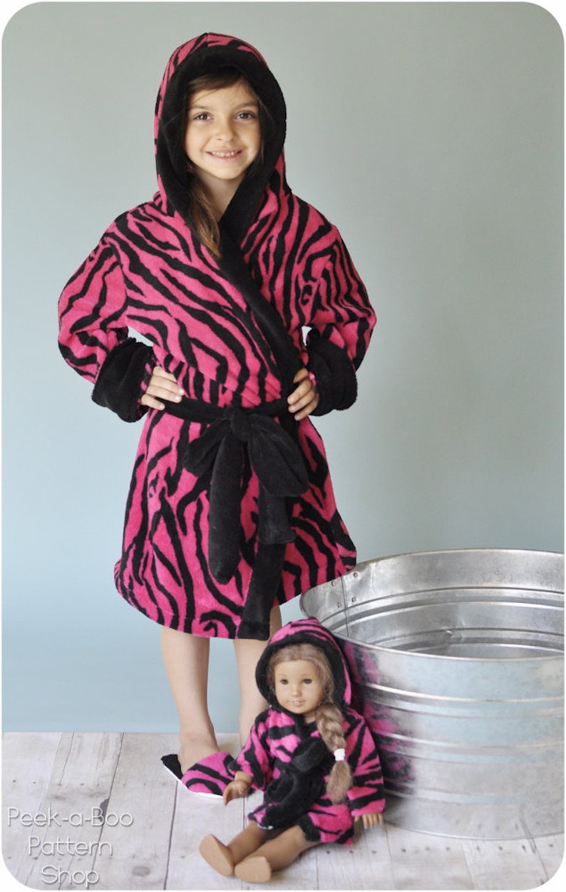 May include: A pink and black zebra print robe with a hood and a matching belt. A smaller doll is wearing a similar robe. The text "Peek-a-Boo Pattern Shop" is visible at the bottom of the image.