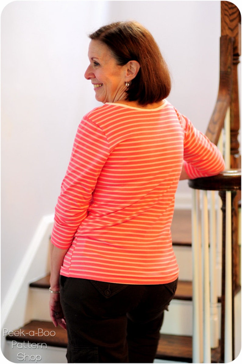 May include: A woman wearing a pink and white striped long-sleeved shirt and black pants. She is standing on a staircase and leaning against a railing.