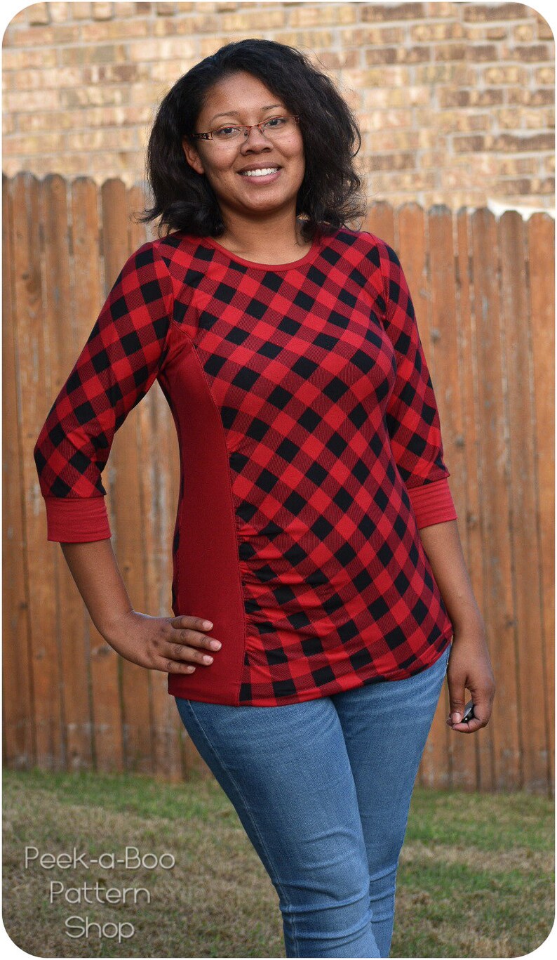May include: A woman wearing a red and black plaid shirt with a red side panel and blue jeans. The shirt has a diamond pattern.