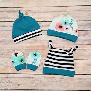 May include: Four baby hats in different patterns. A teal hat with a white stripe, a teal hat with a floral pattern, a teal hat with black and white stripes, and a pair of teal mittens with a floral pattern.