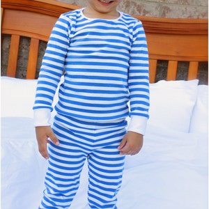 Puede incluir: Un ni&ntilde;o peque&ntilde;o con un pijama a rayas azul y blanco. Est&aacute; de pie sobre una colcha blanca con una manta de ganchillo blanca debajo.