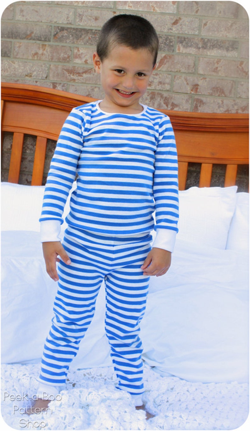 Puede incluir: Un ni&ntilde;o peque&ntilde;o con un pijama a rayas azul y blanco. Est&aacute; de pie sobre una colcha blanca con una manta de ganchillo blanca debajo.