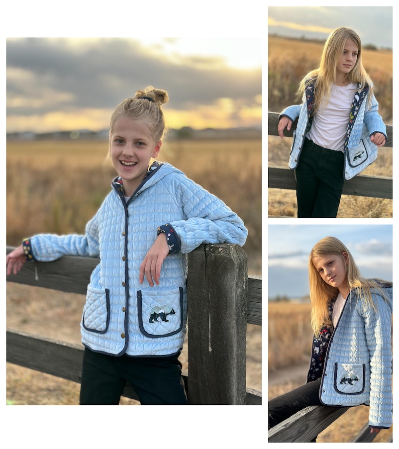 May include: A light blue quilted jacket with a hood and a bear design on the pocket. The jacket has a button closure and navy blue trim.