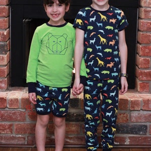 Puede incluir: Dos ni&ntilde;os con pijamas. La ni&ntilde;a lleva una camisa verde de manga larga con un dise&ntilde;o de oso geom&eacute;trico y pantalones cortos con estampado azul y blanco. El ni&ntilde;o lleva una camisa azul marino de manga corta con estampado de animales de colores y pantalones azules a juego con el mismo estampado de animales.