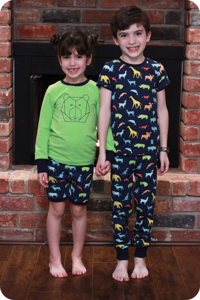 Puede incluir: Dos ni&ntilde;os con pijamas. La ni&ntilde;a lleva una camisa verde de manga larga con un dise&ntilde;o de oso geom&eacute;trico y pantalones cortos con estampado azul y blanco. El ni&ntilde;o lleva una camisa azul marino de manga corta con estampado de animales de colores y pantalones azules a juego con el mismo estampado de animales.