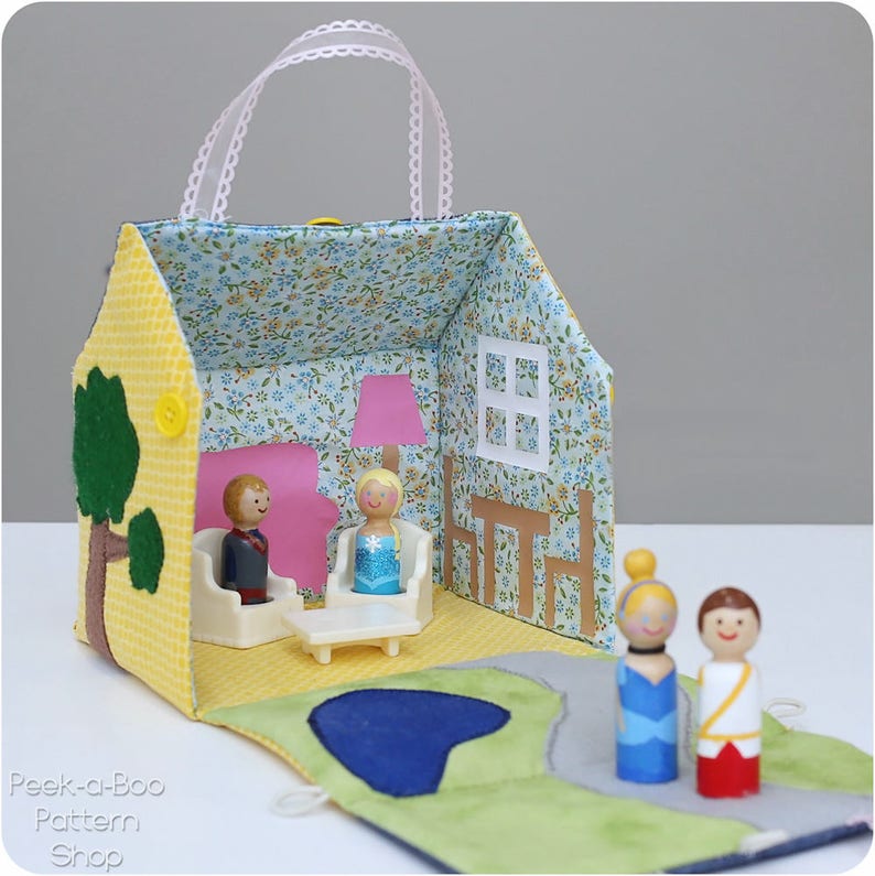 Peut inclure: Une maison de poup&eacute;e en feutre jaune avec un int&eacute;rieur &agrave; motifs floraux bleu et blanc. La maison de poup&eacute;e a une poign&eacute;e et s'ouvre pour r&eacute;v&eacute;ler un salon avec des meubles et deux poup&eacute;es. La maison de poup&eacute;e est pos&eacute;e sur un tapis en feutre vert et bleu avec un &eacute;tang.