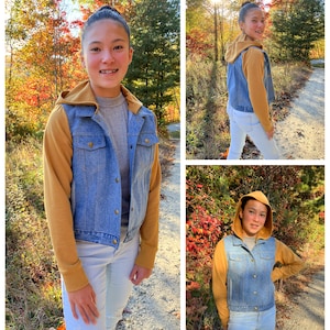 May include: A denim jacket with a mustard-colored hood and sleeves. The jacket has a button-up front and is worn over a gray shirt and light-wash jeans. The background features a path and trees with fall foliage.