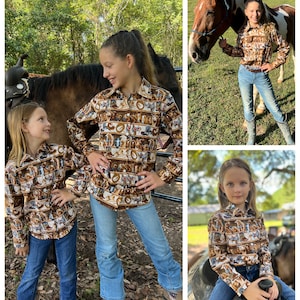 Puede incluir: Dos chicas con camisas de manga larga de color marr&oacute;n, blanco y azul con estampado de caballos y tem&aacute;tica western. Una chica est&aacute; de pie junto a un caballo marr&oacute;n, mientras que la otra chica est&aacute; sentada en un caballo marr&oacute;n.