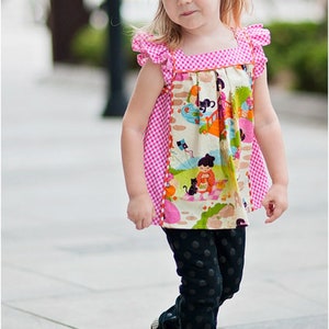 May include: A young girl wearing a pink and white gingham top with a colorful print and black polka dot pants. She is wearing white shoes with black accents.