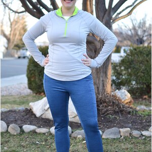 May include: A woman wearing athletic apparel, including a light gray long-sleeve top with a neon green collar and zipper, and blue leggings. She is also wearing pink and black athletic shoes. The image includes the text "Peek-a-Boo Pattern Shop".
