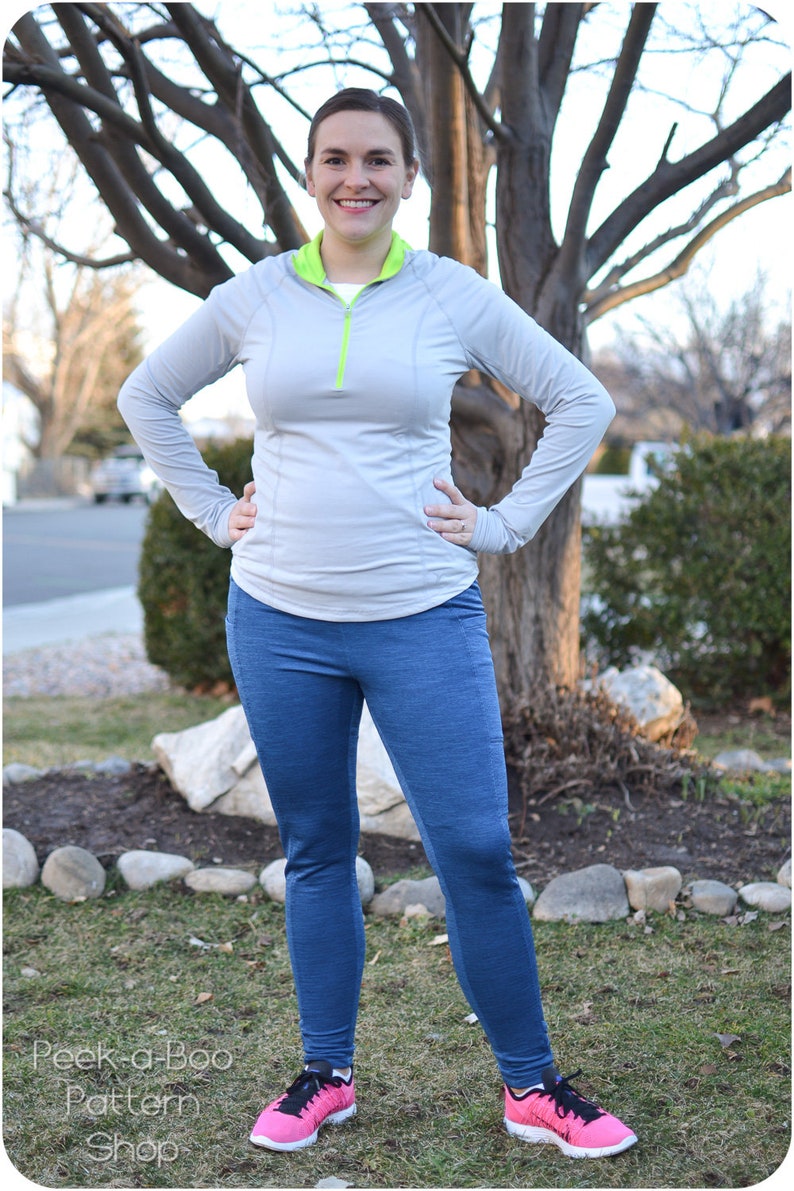 May include: A woman wearing athletic apparel, including a light gray long-sleeve top with a neon green collar and zipper, and blue leggings. She is also wearing pink and black athletic shoes. The image includes the text "Peek-a-Boo Pattern Shop".