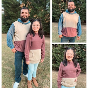 May include: A family of three wearing matching two-toned hoodies. The hoodies are beige and burgundy with a kangaroo pocket on the front. The family are standing in a grassy area with trees in the background.