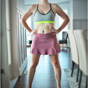 May include: A woman wearing a gray sports bra with a neon green band and a pink athletic skirt. The image also shows a dark wood floor and the text "Peek-a-Boo Pattern Shop".