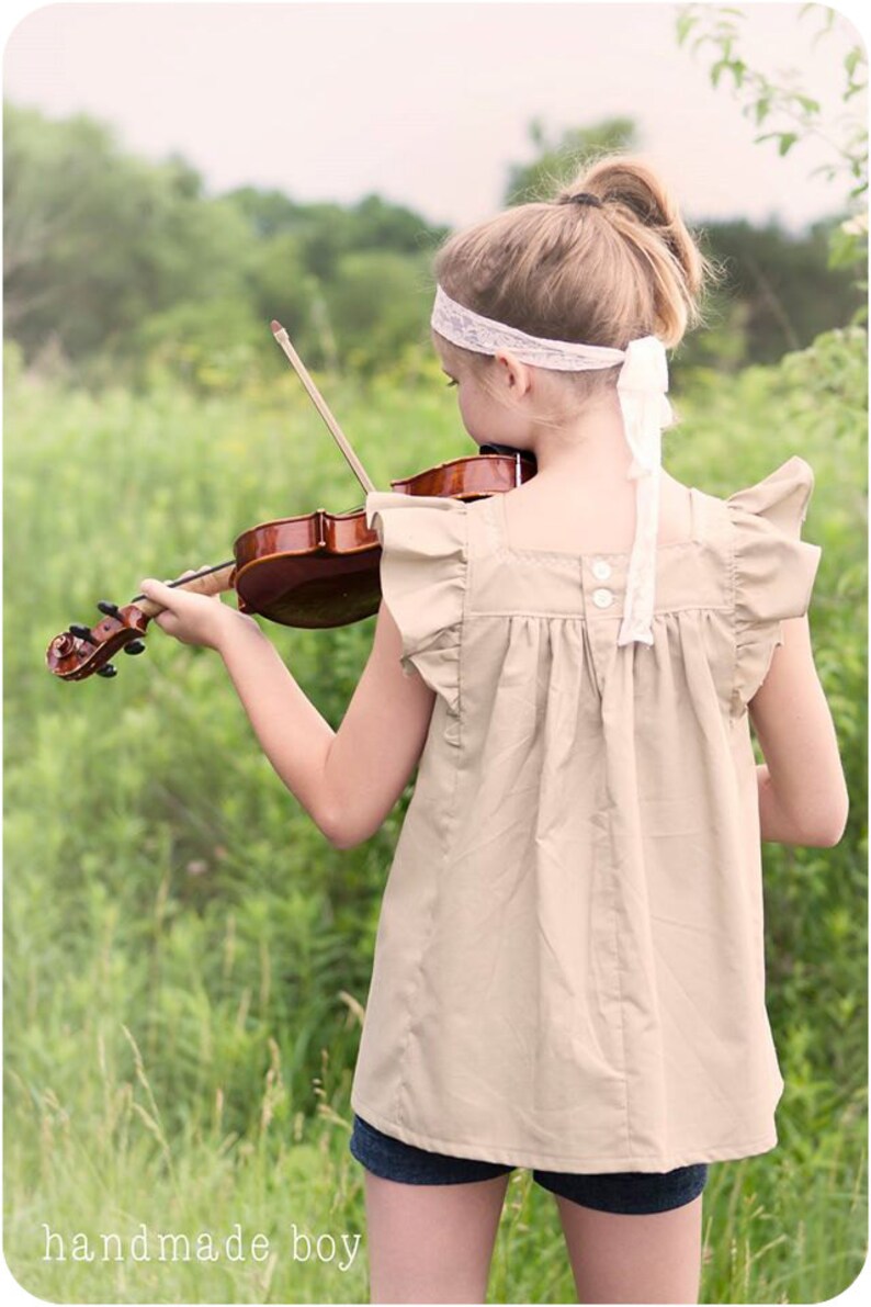 May include: A young person wearing a beige top with ruffled sleeves and a white headband plays a violin in a field of green grass.
