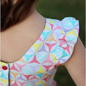 May include: A girl's dress with a colorful geometric pattern and ruffled sleeves. The dress has a button closure at the back of the neck. The text "Peek-a-Boo Pattern Shop" is visible at the bottom of the image.