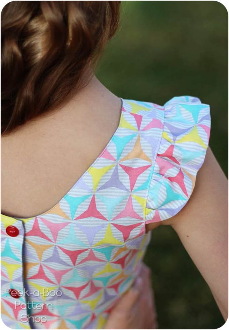 May include: A girl's dress with a colorful geometric pattern and ruffled sleeves. The dress has a button closure at the back of the neck. The text "Peek-a-Boo Pattern Shop" is visible at the bottom of the image.