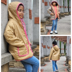 May include: A quilted jacket with a hood, featuring a gold colour with pink trim. The jacket has a zip closure and pockets. The model is wearing blue jeans.