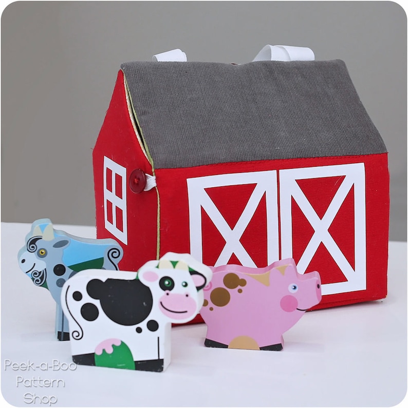 Peut inclure: Une grange rouge avec des portes et des fen&ecirc;tres blanches, et un toit gris. Il y a quatre figurines d'animaux en bois devant la grange : une ch&egrave;vre grise, une vache noire et blanche, un cochon rose et une vache brune et blanche.