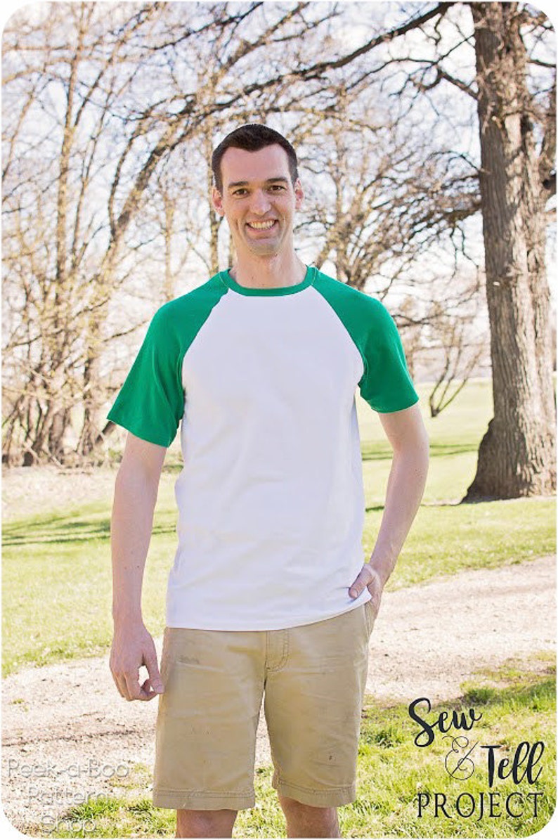 May include: A man wearing a white and green baseball tee shirt with khaki shorts. He is standing in a grassy area with trees in the background. The text "Sew & Tell Project" is visible in the lower right corner of the image.