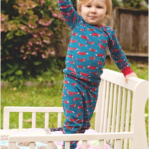 Puede incluir: Un ni&ntilde;o peque&ntilde;o con un pijama de manga larga azul y rojo con estampado de zorro se para en una cama de madera blanca para ni&ntilde;os peque&ntilde;os. La cama tiene una colcha de retazos colorida.