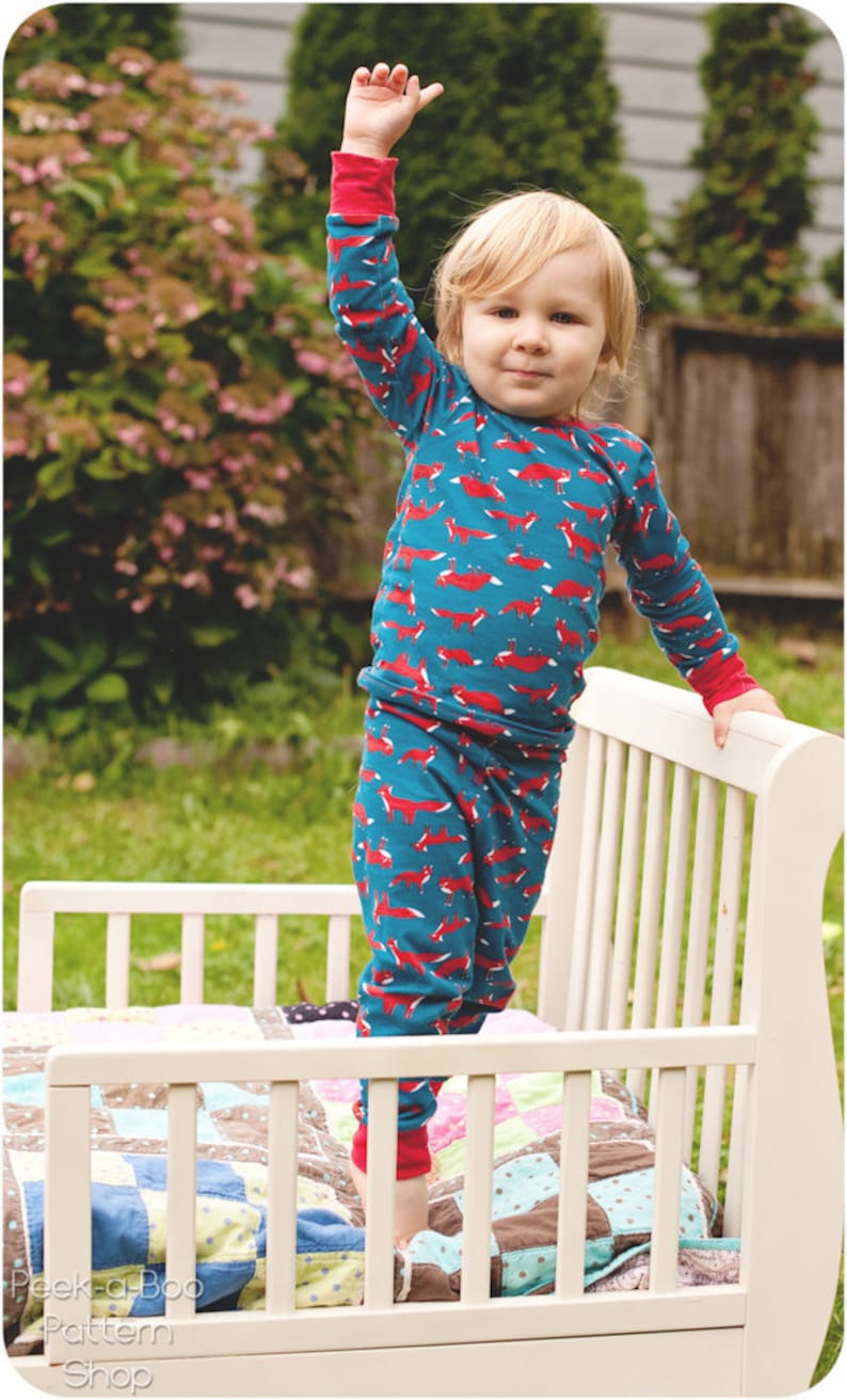 Puede incluir: Un ni&ntilde;o peque&ntilde;o con un pijama de manga larga azul y rojo con estampado de zorro se para en una cama de madera blanca para ni&ntilde;os peque&ntilde;os. La cama tiene una colcha de retazos colorida.