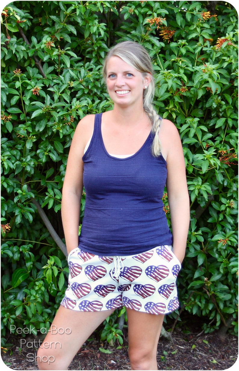 Pu&ograve; includere: Una donna indossa una canotta blu navy e pantaloncini bianchi con un motivo a cuore rosso, bianco e blu. I pantaloncini hanno una vita con coulisse.