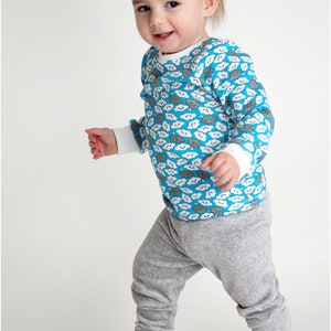 Puede incluir: Un ni&ntilde;o peque&ntilde;o con una camisa azul de manga larga con un estampado de nubes blancas y pantalones de ch&aacute;ndal grises. La camisa tiene un cuello redondo y los pantalones de ch&aacute;ndal tienen un corte holgado.