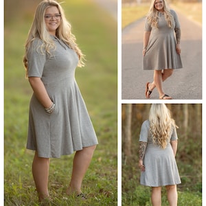 Pode incluir: Uma mulher vestindo um vestido cinza de manga curta com capuz, com um corpete justo e uma saia rodada. O vestido tem um bolso do lado esquerdo. A mulher est&aacute; em p&eacute; em um campo gramado.