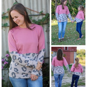 May include: Two people wearing pink and grey long-sleeved shirts with a leopard print pattern on the sleeves. The shirts are a split design with a solid pink top and a leopard print bottom. The people are wearing blue jeans.