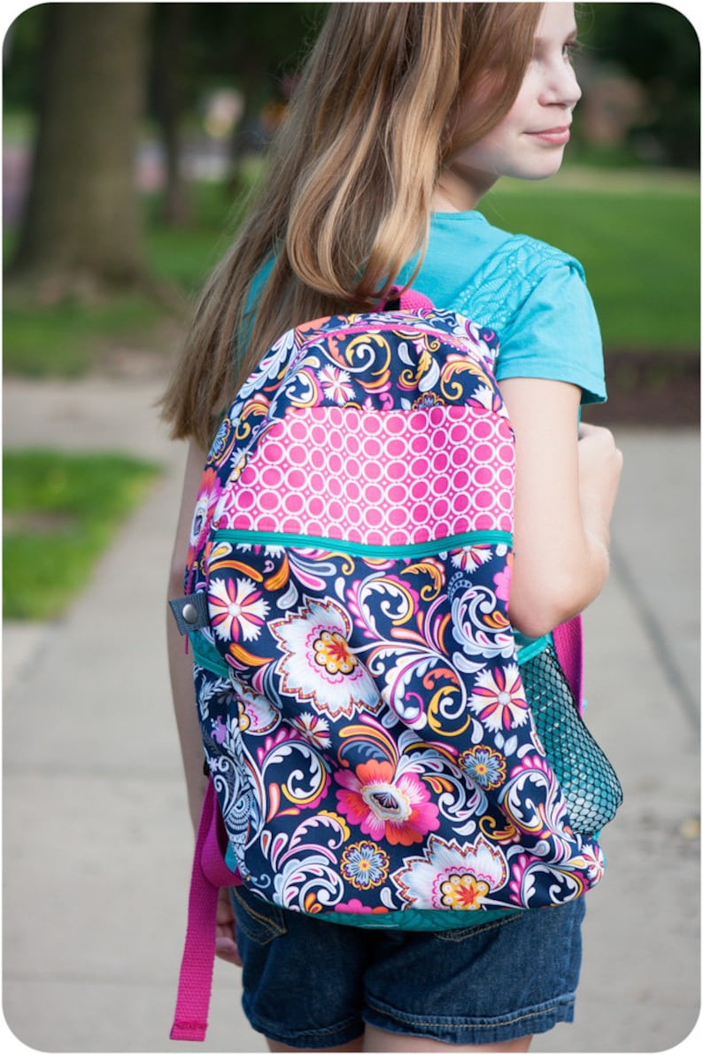 May include: A colorful backpack with a floral pattern in shades of pink, blue, and yellow. The backpack has a mesh pocket on the side and a zippered pocket on the front.