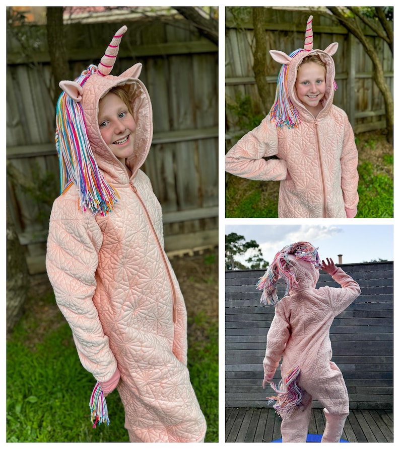 May include: A pink unicorn onesie with a rainbow mane and tail. The onesie has a zipper down the front and a hood with unicorn ears. The child wearing the onesie is smiling and looking at the camera.