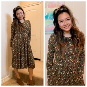 Pode incluir: Uma mulher vestindo um vestido midi verde floral com mangas compridas e decote redondo. Ela est&aacute; usando botas de tornozelo marrons e tem uma faixa de cabelo.