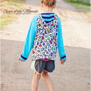 May include: A young person wearing a blue and white hooded sweatshirt with a colorful animal print design. The sweatshirt has a blue and white striped band around the neck. The person is wearing black shorts and pink and black sneakers. The person is walking on a gravel path.