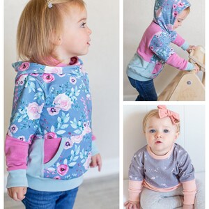 May include: Two toddlers wearing different styles of hooded sweatshirts. The first sweatshirt is blue with a floral print and pink accents. The second sweatshirt is gray with a floral print and pink accents.