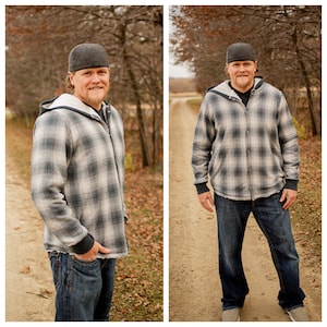 May include: A man wearing a gray and white plaid hooded shirt with a gray baseball cap. He is standing in a wooded area with a dirt path in front of him.