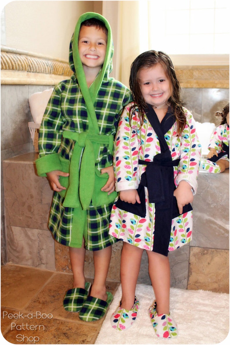 May include: Two children wearing matching green and blue plaid and floral print robes with matching slippers. The robes have a hood and a tie belt. The slippers are green and blue plaid and floral print.