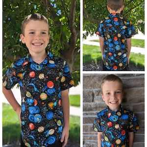 Puede incluir: Un ni&ntilde;o lleva una camisa de manga corta con botones de color azul, negro y naranja con un estampado de tem&aacute;tica espacial. La camisa tiene planetas, estrellas y remolinos.