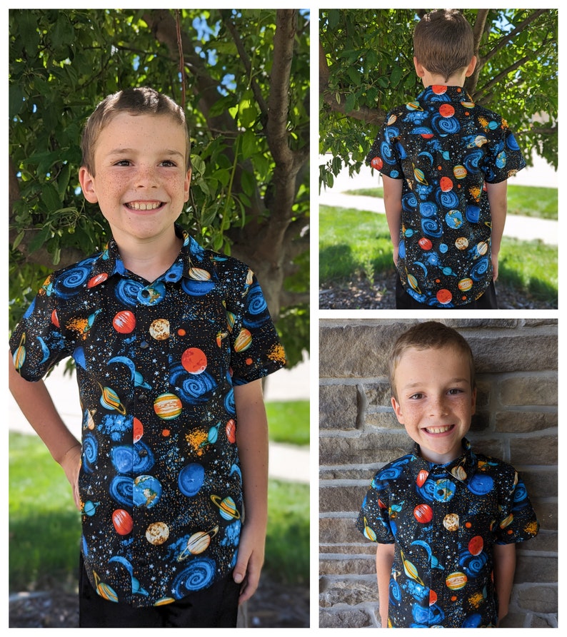 Puede incluir: Un ni&ntilde;o lleva una camisa de manga corta con botones de color azul, negro y naranja con un estampado de tem&aacute;tica espacial. La camisa tiene planetas, estrellas y remolinos.