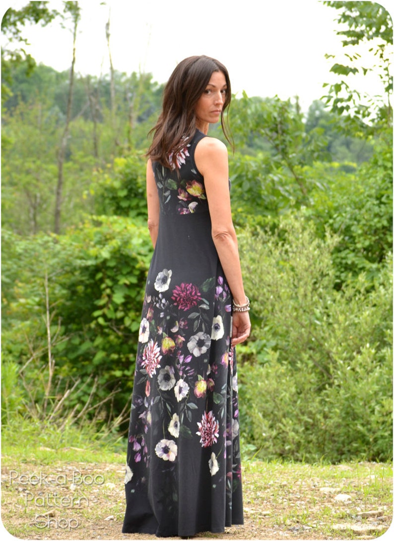 May include: A woman wearing a sleeveless maxi dress with a floral print. The dress is black with a variety of colorful flowers, including pink, purple, white, and yellow. The dress has a fitted bodice and a flowing skirt.