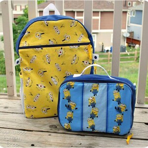 May include: A yellow and blue backpack and lunch bag with a Minion pattern. The backpack has a mesh side pocket and a zippered front pocket. The lunch bag has a blue and white striped background.