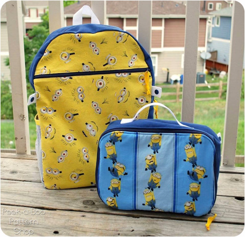 May include: A yellow and blue backpack and lunch bag with a Minion pattern. The backpack has a mesh side pocket and a zippered front pocket. The lunch bag has a blue and white striped background.