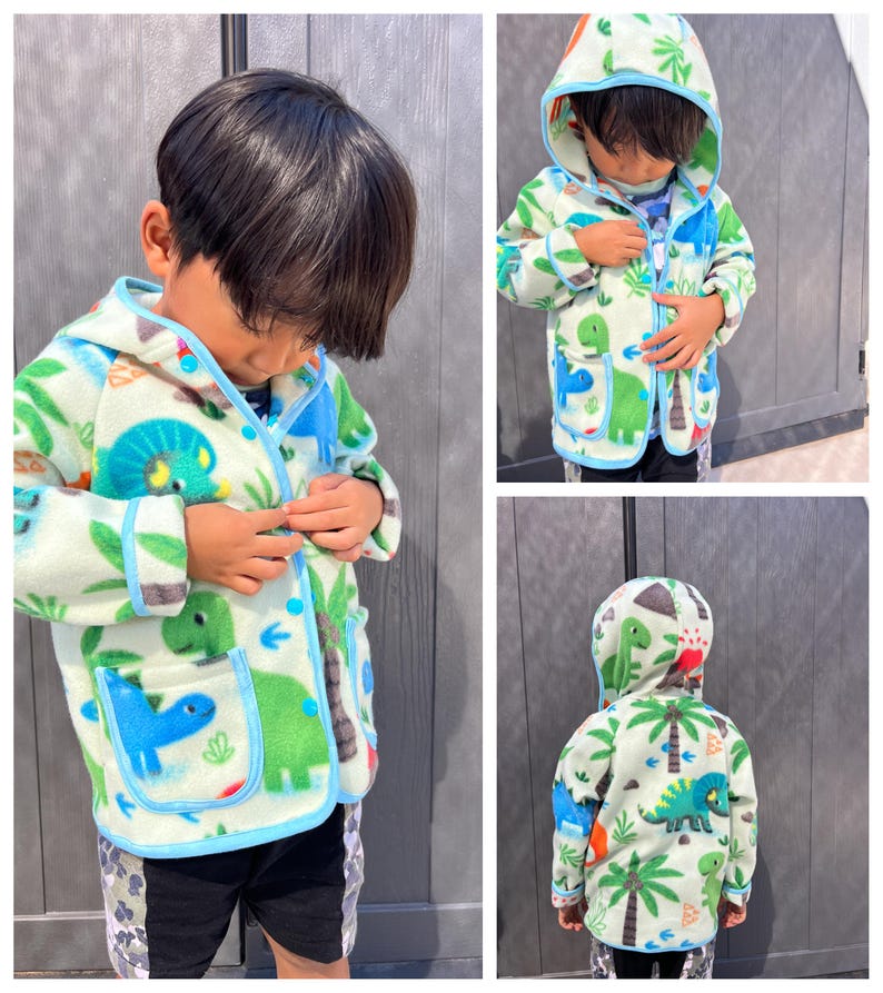May include: A light green fleece jacket with a blue trim and a dinosaur print. The jacket has a hood and a front zip closure.