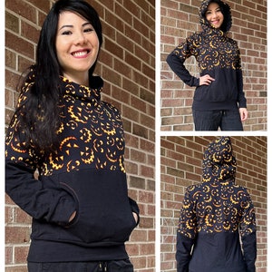 May include: A black and orange hoodie with a pumpkin face pattern on the top half and a solid black bottom half. The hoodie has a hood and a kangaroo pocket.