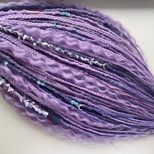 Puede incluir: Un conjunto de rastas lavanda y moradas oscuras, con diversas texturas y elementos decorativos. Se entrelazan secciones trenzadas, mechones ondulados y mechones lisos. Los adornos incluyen pequeñas cuentas, detalles florales y colgantes de media luna plateados.